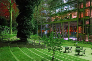 Jardin nocturne avec bâtiment moderne en verre.